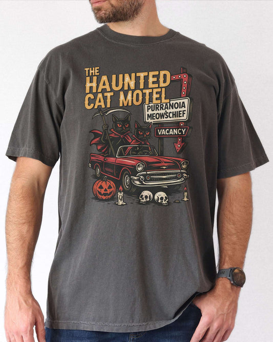 Man wearing a pepper-colored 'The Haunted Cat Motel' shirt with a funny retro Halloween graphic of two cats driving to a spooky motel.