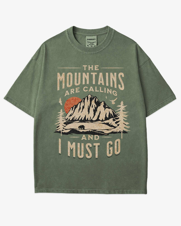Flat lay moss shirt with phrase ‘The Mountains Are Calling And I Must Go’ and retro mountain nature graphic.