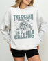 Model wearing ash color sweatshirt with 'The Ocean Is Calling' graphic design