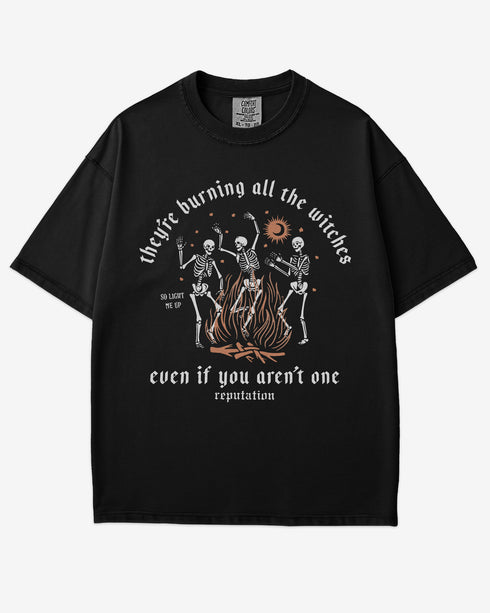They’re Burning All The Witches Shirt – flat lay black tee with funny retro skeletons dancing in fire graphic