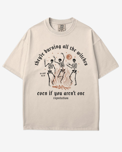 They’re Burning All The Witches Shirt – flat lay ivory tee with funny retro skeletons dancing in fire graphic