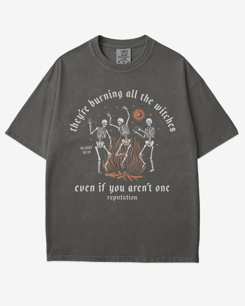 They’re Burning All The Witches Shirt – flat lay pepper tee with funny retro skeletons dancing in fire graphic
