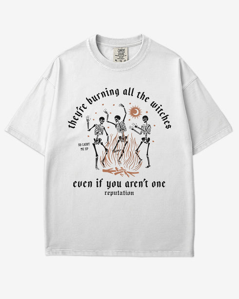 They’re Burning All The Witches Shirt – flat lay white tee with funny retro skeletons dancing in fire graphic