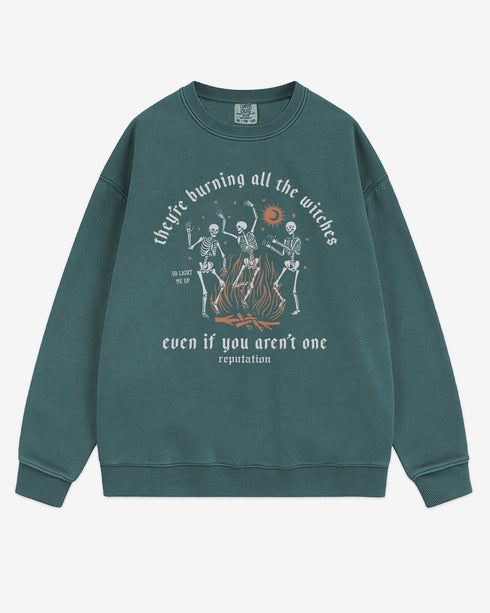 They’re Burning All The Witches Sweatshirt flat lay blue spruce color retro graphic with skeletons dancing in fire