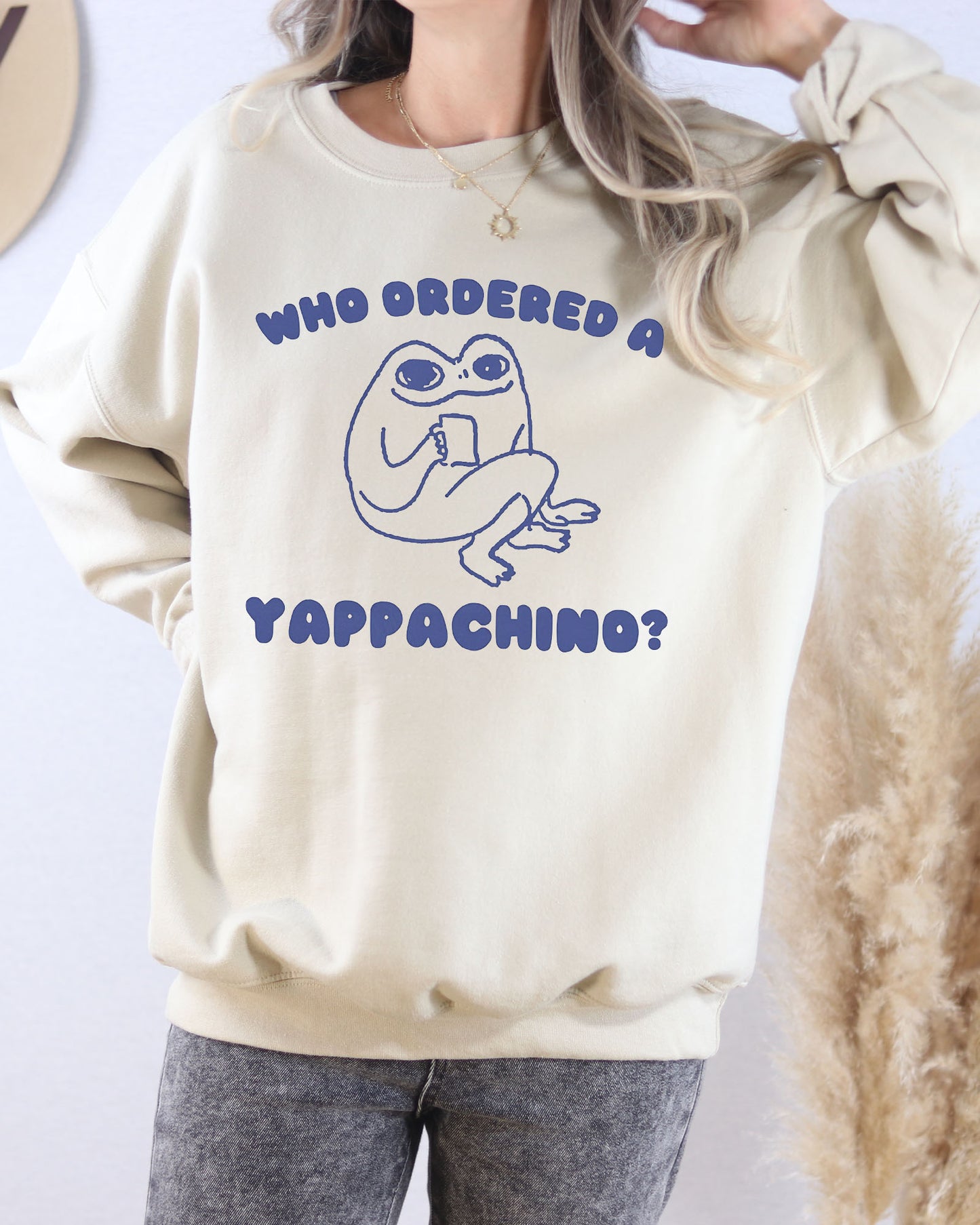 Model wearing sand color sweatshirt with 'Who Ordered A Yappachino' graphic design