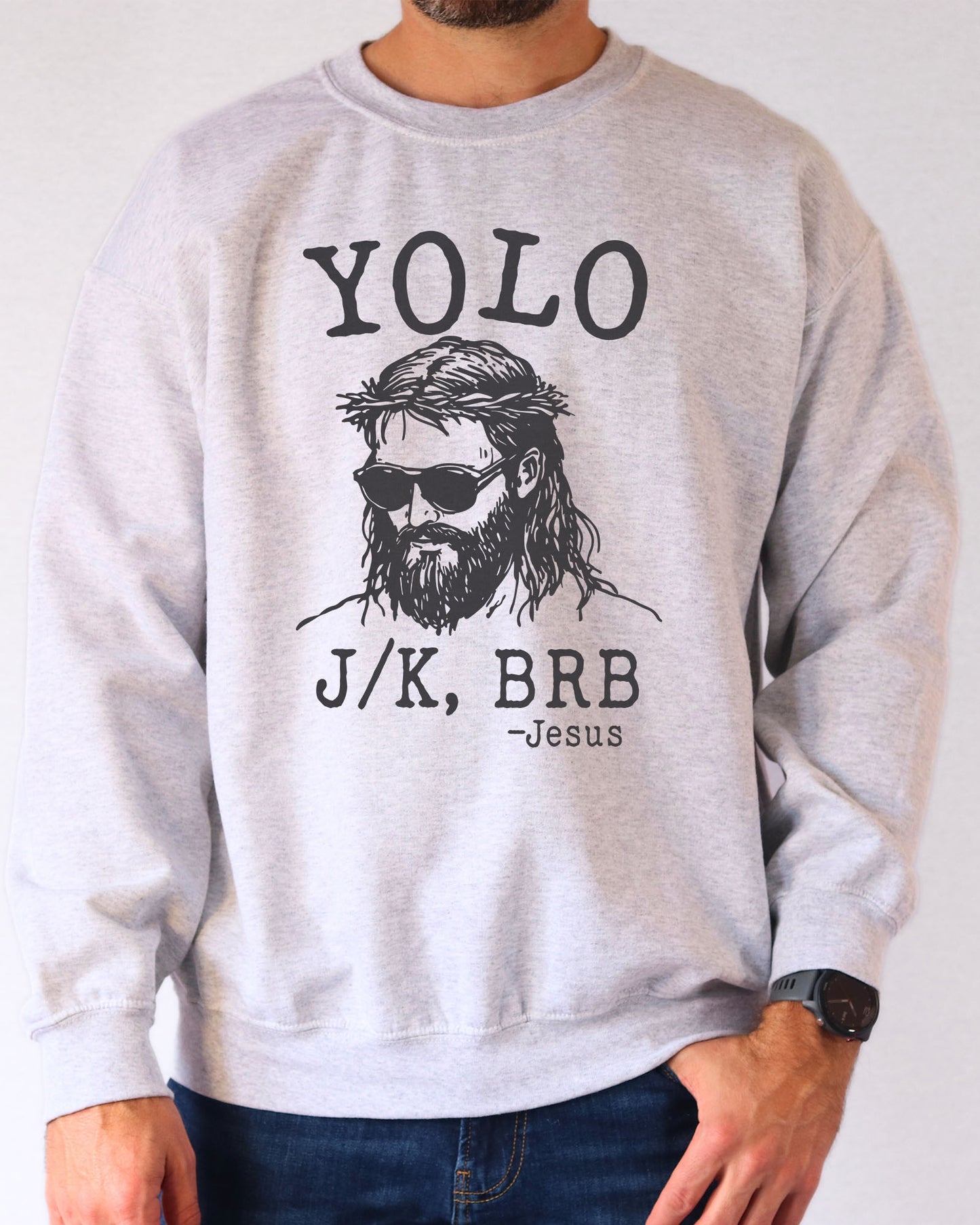 Model wearing ash color sweatshirt with 'YOLO Jesus J/K BRB' graphic design