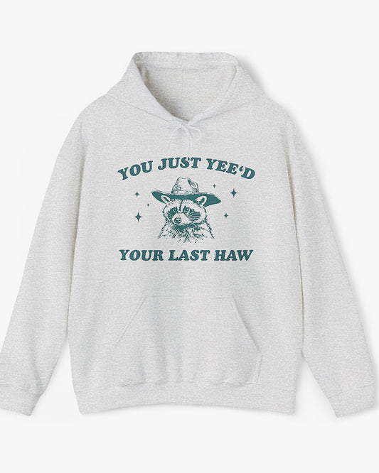 Flat laying ash gray 'You Just Yeed Your Last Haw' hoodie with funny cowboy raccoon graphic