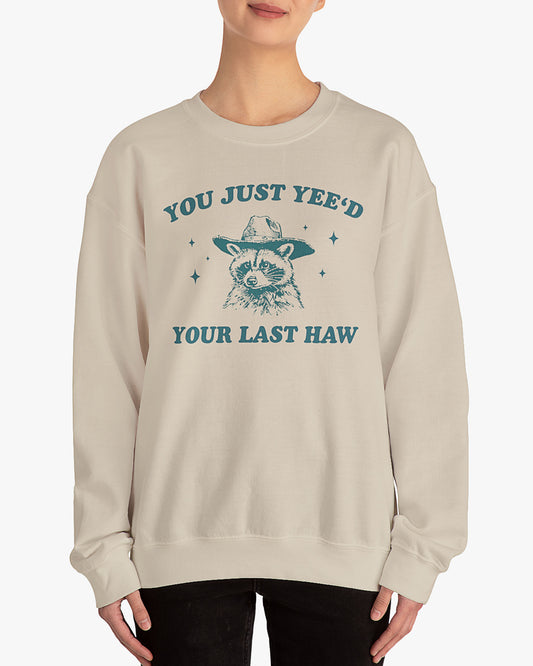 Woman wearing sand beige 'You Just Yeed Your Last Haw' sweatshirt with funny retro cowboy raccoon graphic