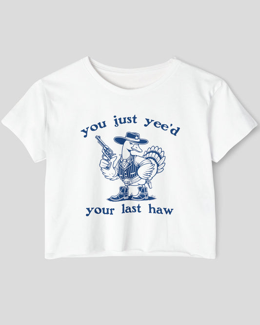 Flat lay of a white 'You Just Yee'd Your Last Haw' crop top featuring a funny retro cowboy goose graphic.