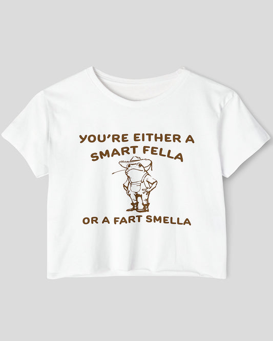 Flat lay white-colored 'You're Either A Smart Fella Or A Fart Smella' crop top featuring a funny retro cowboy frog graphic.