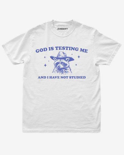 God Is Testing Me And I Have Not Studied shirt in white with cowboy raccon graphic