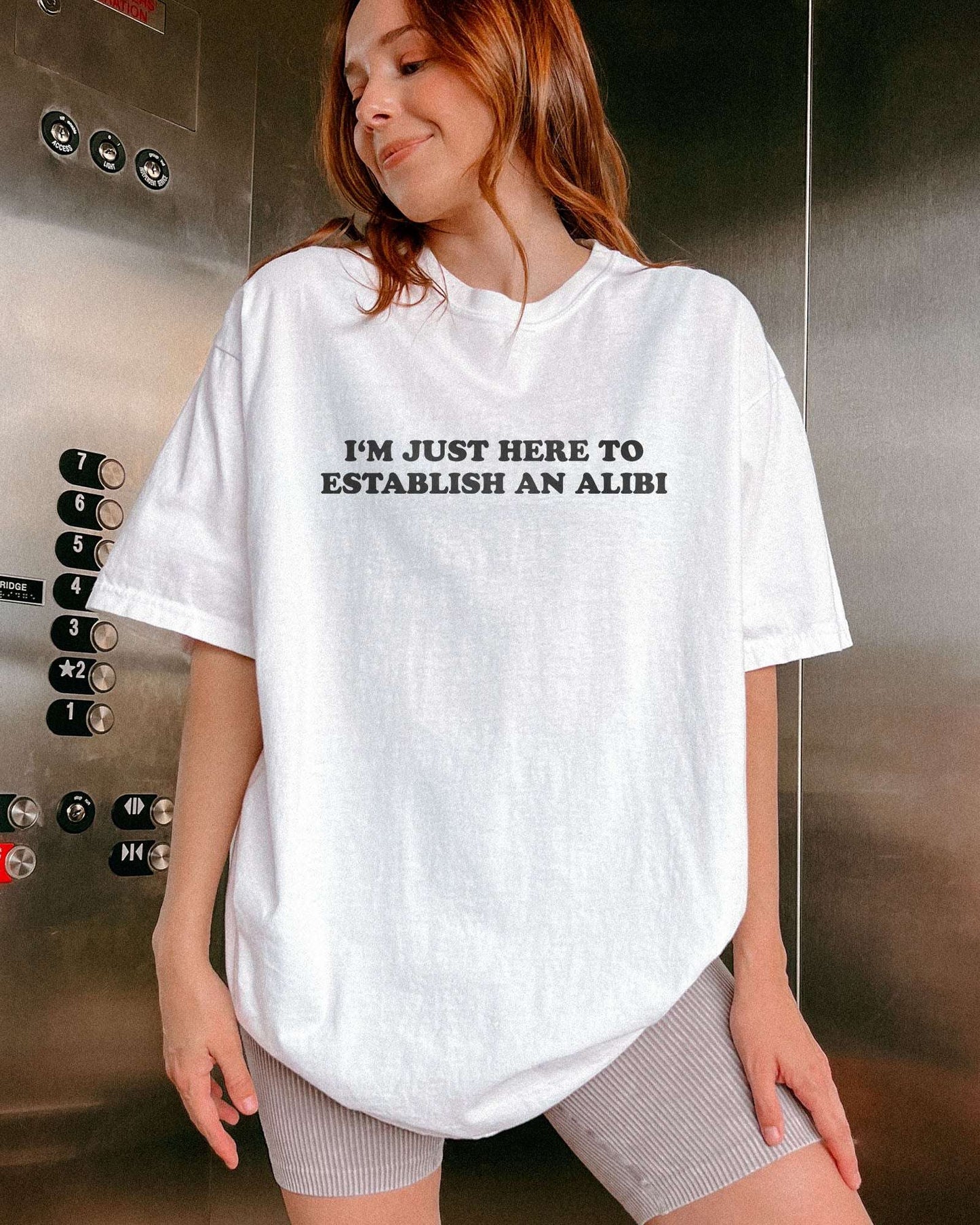 Woman wearing a white I'm Just Here To Establish An Alibi shirt.