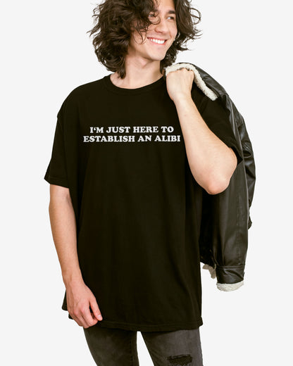 Man wearing a black I'm Just Here To Establish An Alibi shirt.