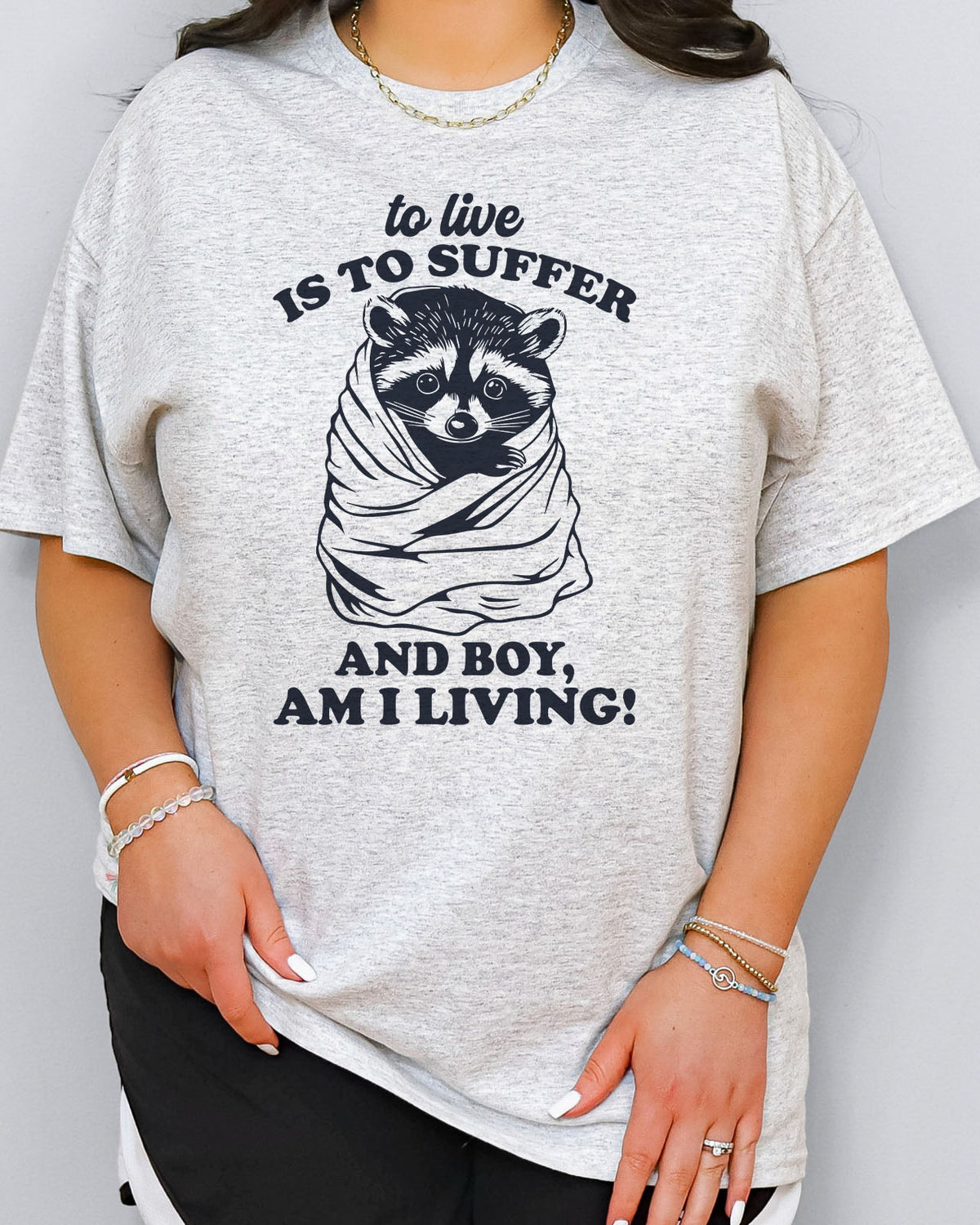 To Live Is To Suffer Shirt in ash grey color with a cute raccoon graphic