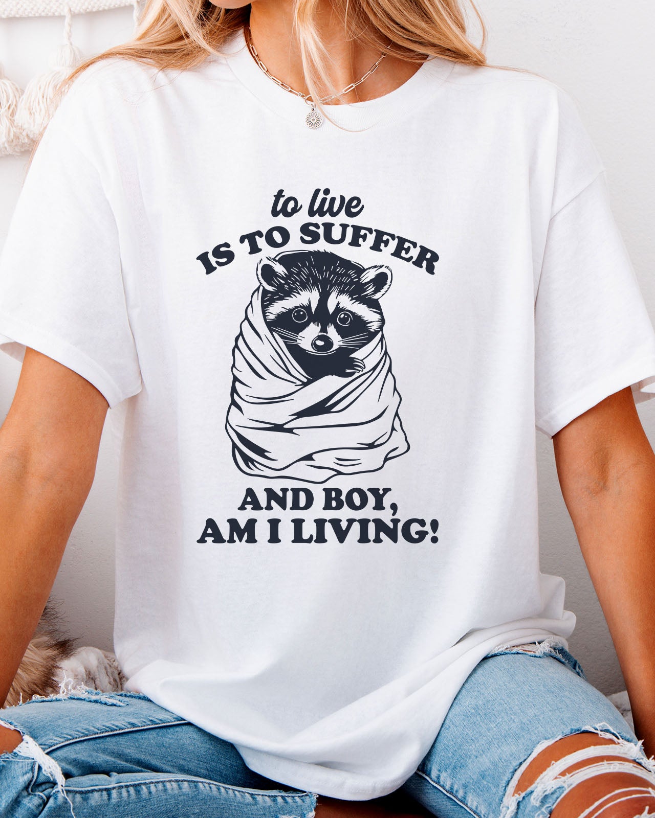 To Live Is To Suffer Shirt in white color with a cute raccoon graphic