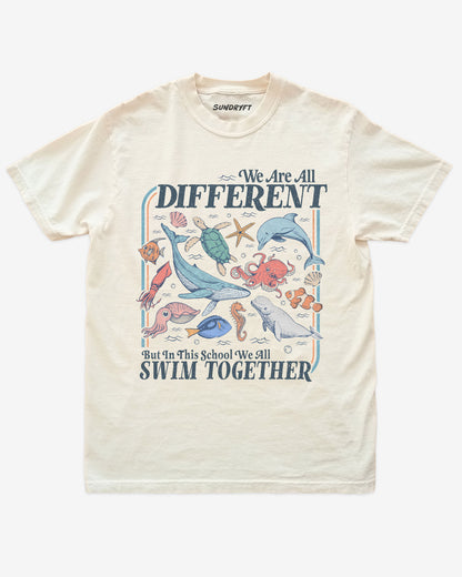 Flat lay of ivory We Are All Different But In This School We All Swim Together Shirt with cute retro ocean animal design