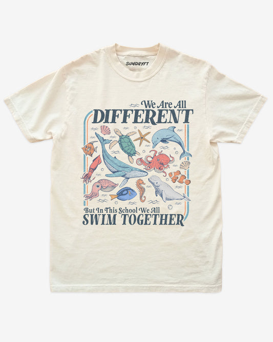 Flat lay of ivory We Are All Different But In This School We All Swim Together Shirt with cute retro ocean animal design