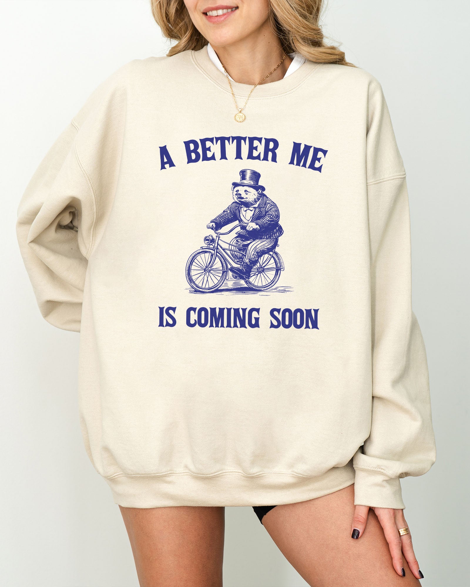 Model wearing sand color sweatshirt with 'A Better Me Is Coming' graphic design