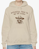 Woman wearing an 'Actually This is My First Rodeo' hoodie in sand beige, featuring a retro western graphic design and unisex fit.