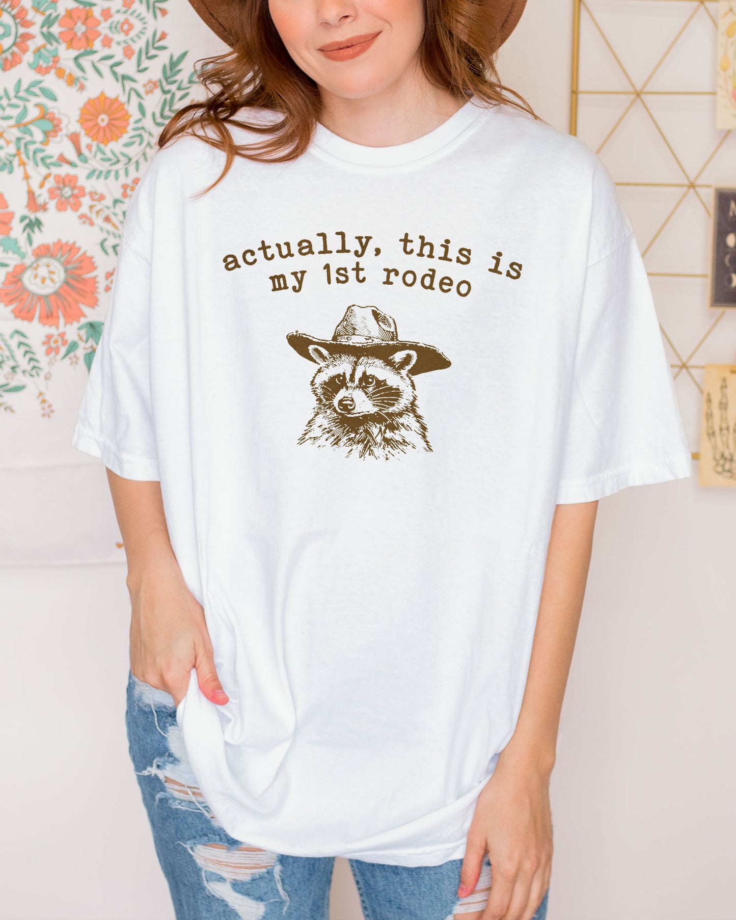 Woman wearing a white 'Actually This Is My First Rodeo' shirt with a funny retro cowboy raccoon.