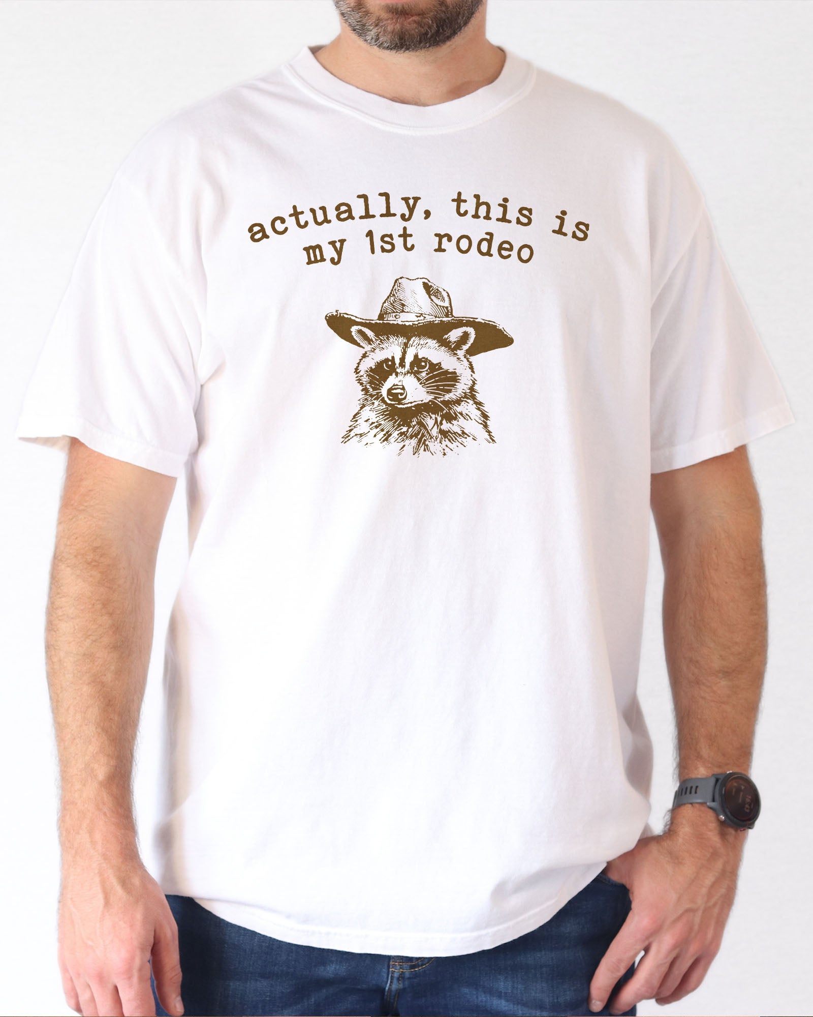 Man wearing a white 'Actually This Is My First Rodeo' shirt with a funny retro cowboy raccoon.