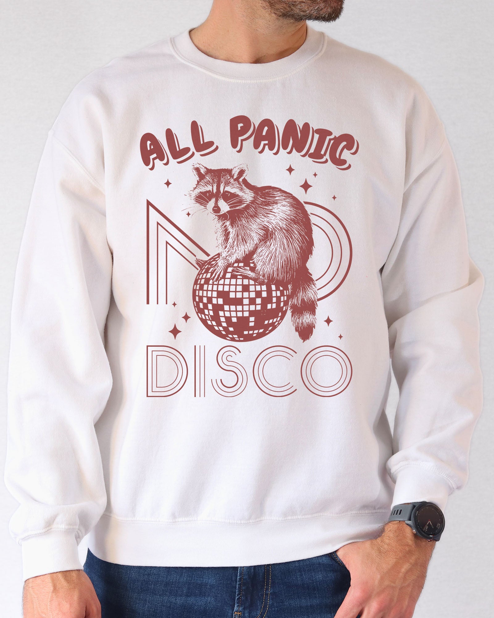 Man wearing a white sweatshirt featuring a funny retro raccoon sitting on a disco ball graphic and the quote 'All Panic No Disco'.