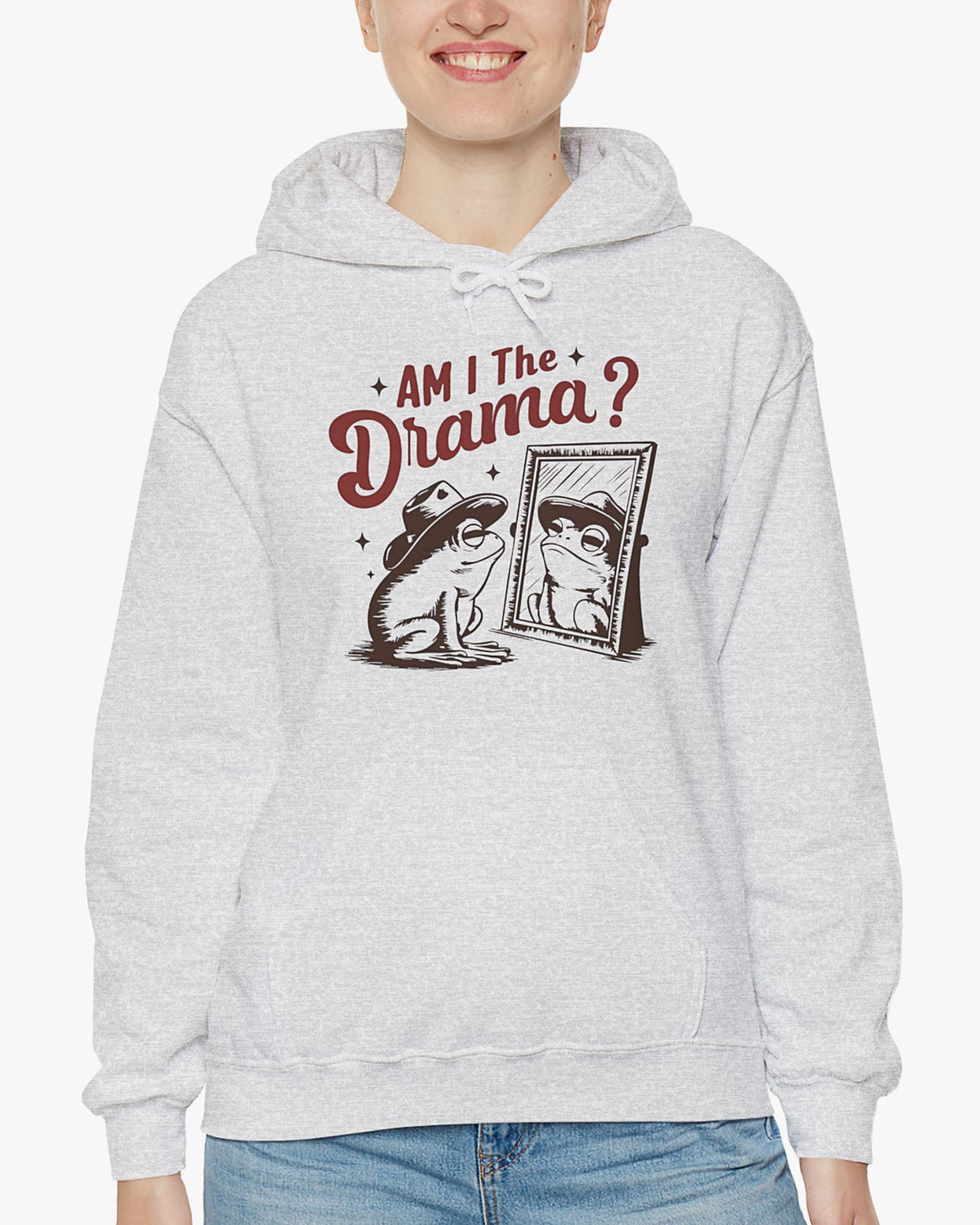 Woman wearing an ash gray 'Am I The Drama?' hoodie featuring a funny retro cowboy frog looking at himself in the mirror graphic.