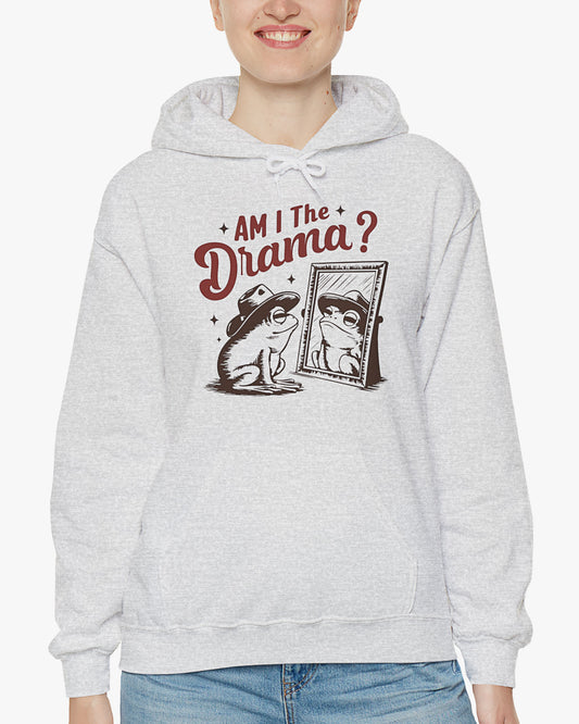 Woman wearing an ash gray 'Am I The Drama?' hoodie featuring a funny retro cowboy frog looking at himself in the mirror graphic.