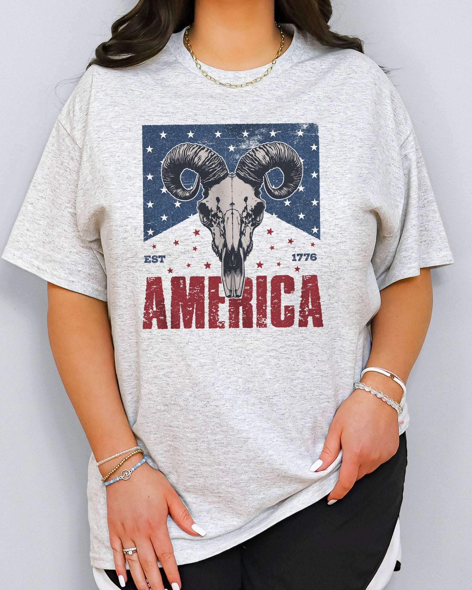 Model wearing ash color shirt with 'America Est 1776' graphic design