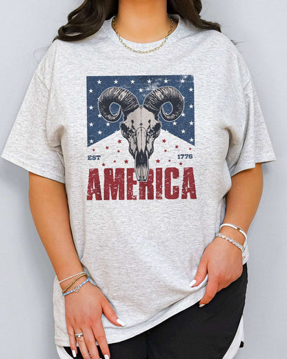 Model wearing ash color shirt with 'America Est 1776' graphic design