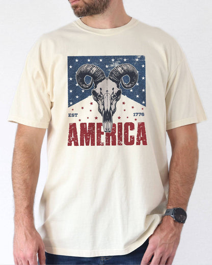 Model wearing natural color shirt with 'America Est 1776' graphic design