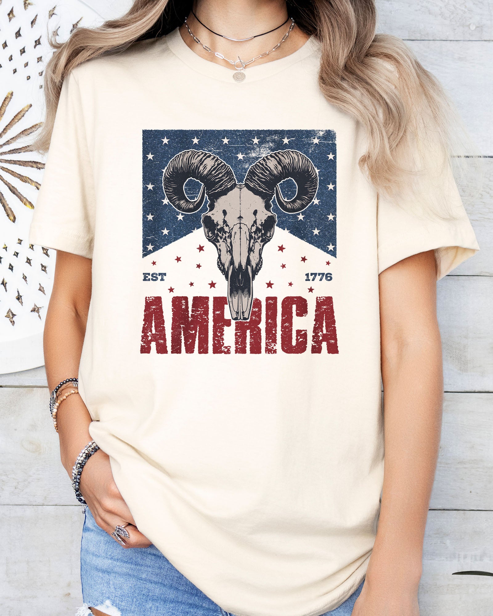 Model wearing natural color shirt with 'America Est 1776' graphic design