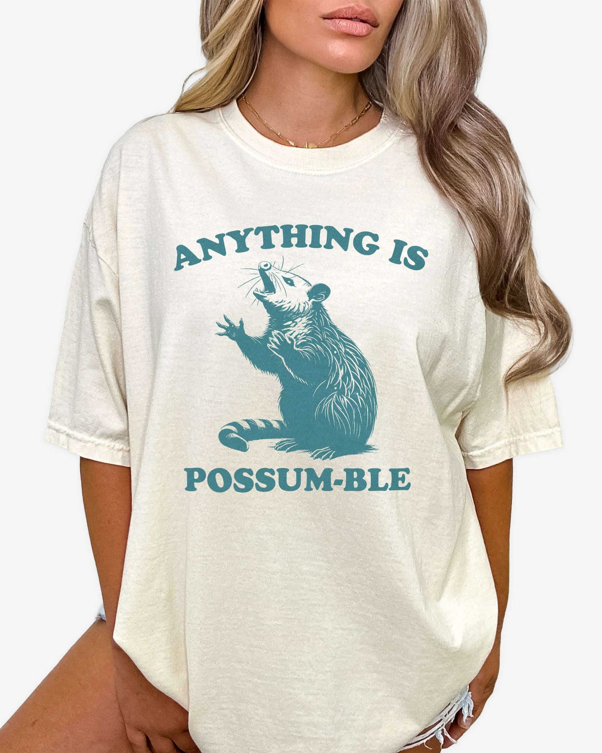 Woman wearing ivory 'Anything Is Possum-ble' shirt with funny retro opossum graphic.