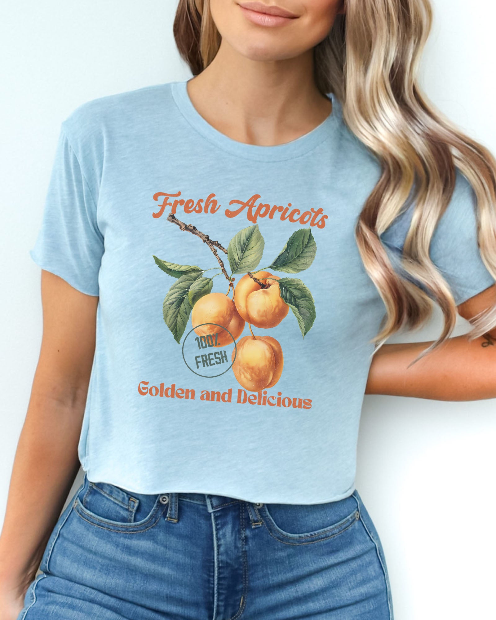 Woman wearing a stonewash denim crop top featuring a retro apricots fruit graphic in a vintage commercial style.