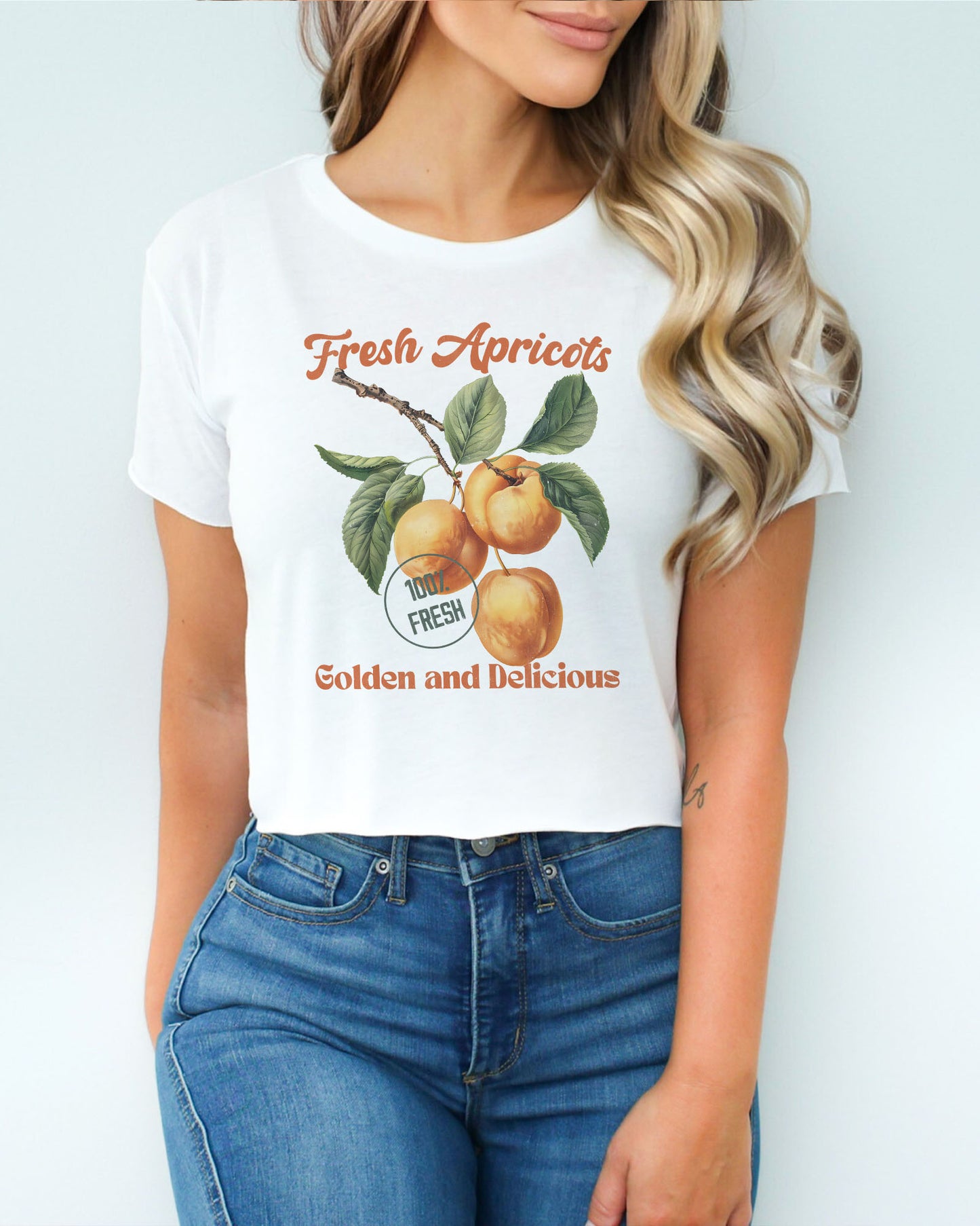 Woman wearing a white crop top featuring a retro apricots fruit graphic in a vintage commercial style.