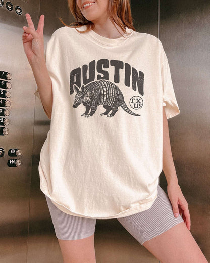 Woman wearing "Austin TX US" shirt in ivory color with retro graphic of an armadillo.