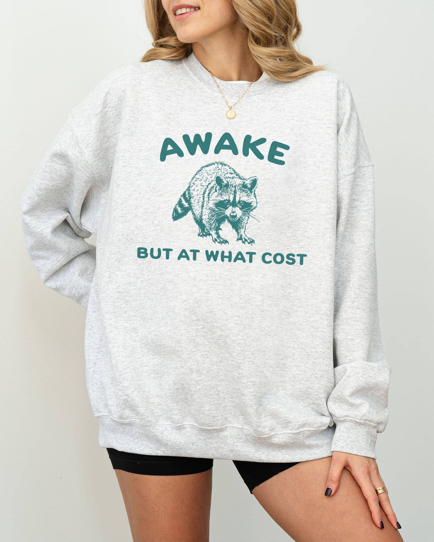 Model wearing ash color sweatshirt with 'Awake, But At What Cost' graphic design