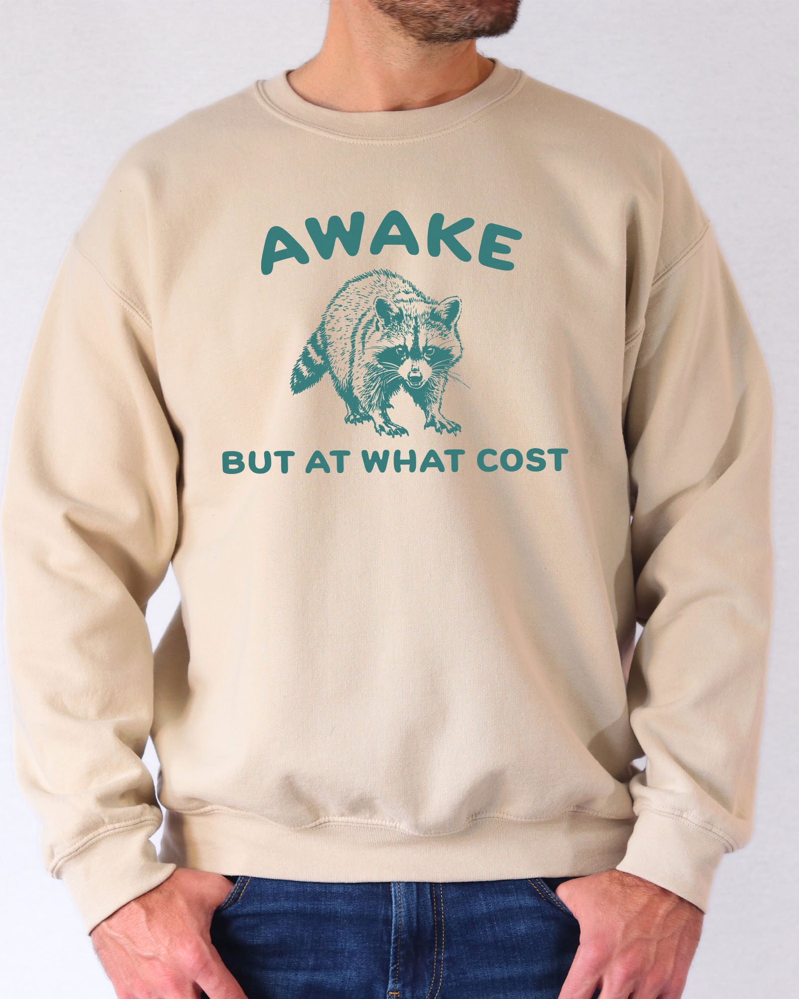 Model wearing sand color sweatshirt with 'Awake, But At What Cost' graphic design