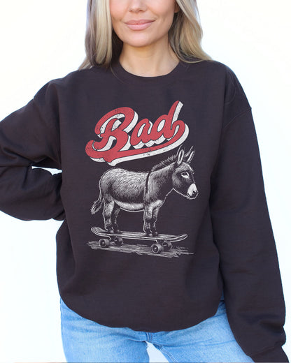Woman wearing a dark chocolate color sweatshirt with a retro graphic of a donkey riding a skateboard and the word 'Bad' above it.