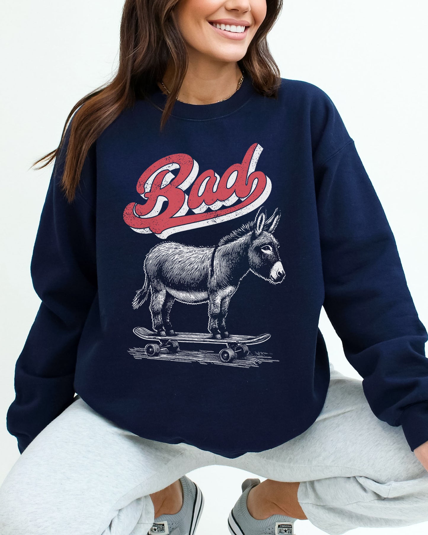 Woman wearing a navy blue sweatshirt with a retro graphic of a donkey riding a skateboard and the word 'Bad' above it.
