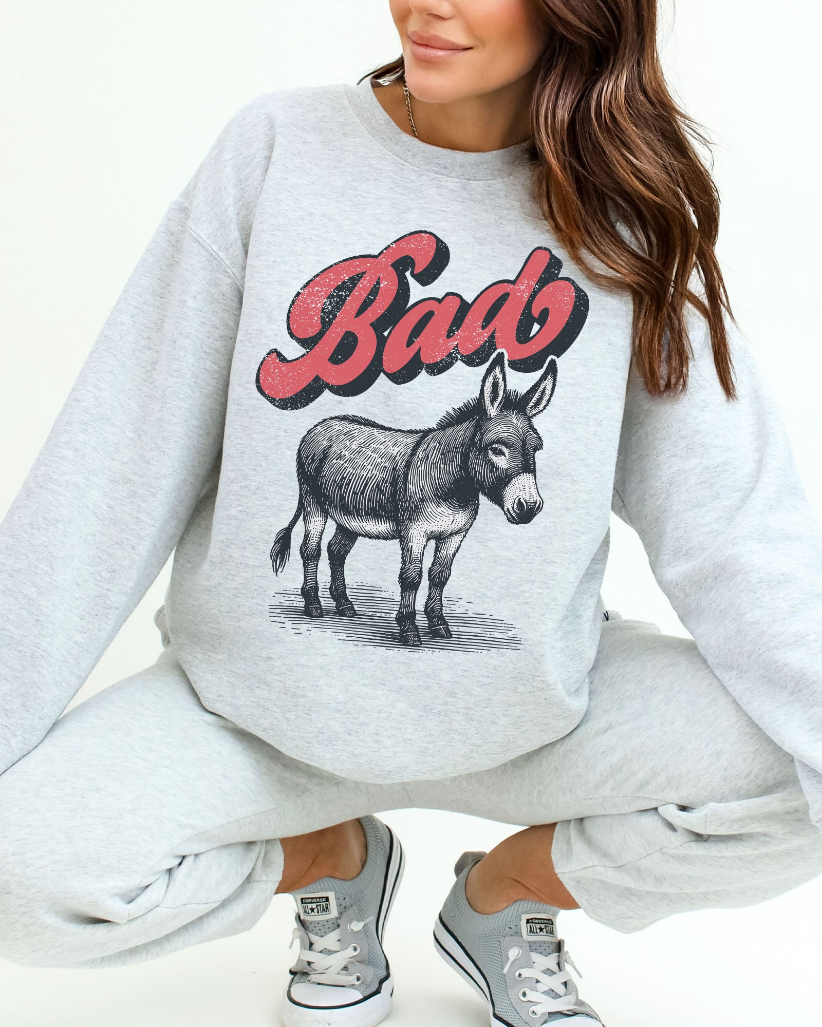 Woman wearing an ash gray unisex retro donkey sweatshirt with the word 'Bad' above the graphic.