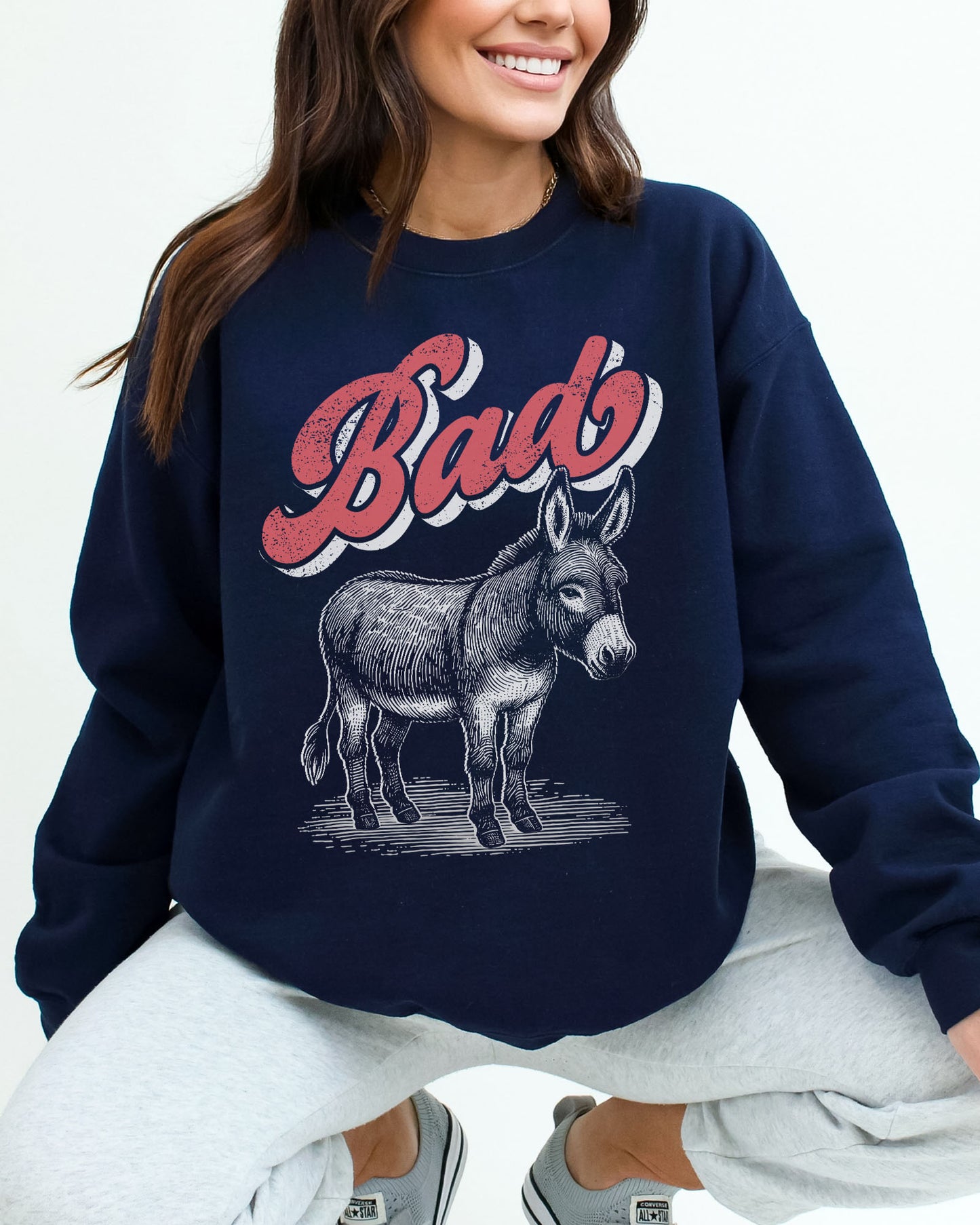 Woman wearing a navy blue unisex retro donkey sweatshirt with the word 'Bad' above the graphic.