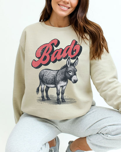 Woman wearing a sand beige unisex retro donkey sweatshirt with the word 'Bad' above the graphic.
