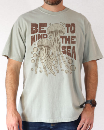 Man wearing a bay "Be Kind To The Sea" shirt with a retro-style graphic of two jellyfish floating underwater.