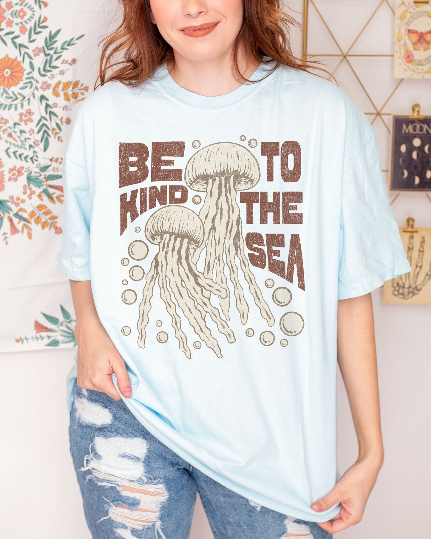 Woman wearing a chambray "Be Kind To The Sea" shirt with a retro-style graphic of two jellyfish floating underwater.