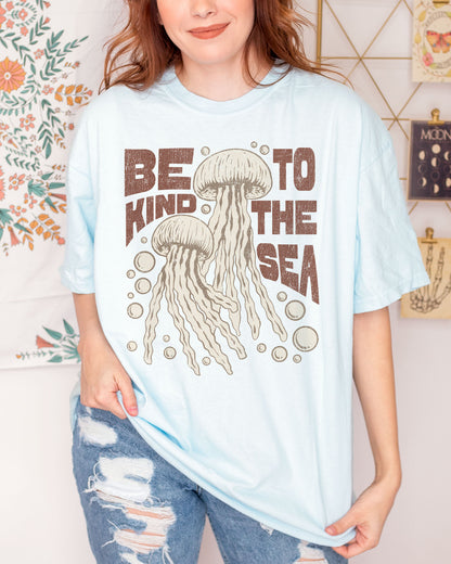 Woman wearing a chambray "Be Kind To The Sea" shirt with a retro-style graphic of two jellyfish floating underwater.