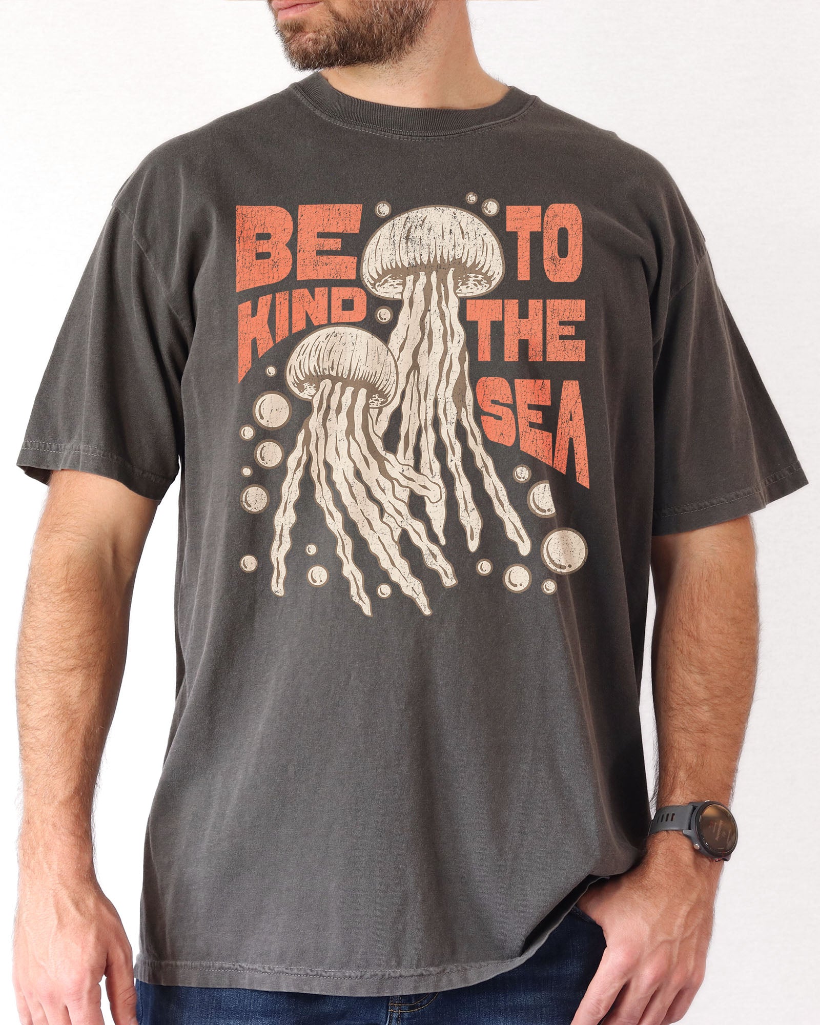 Man wearing a pepper "Be Kind To The Sea" shirt with a retro-style graphic of two jellyfish floating underwater.