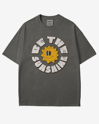 Flat lay pepper-colored Be The Sunshine shirt with a retro boho sun graphic.
