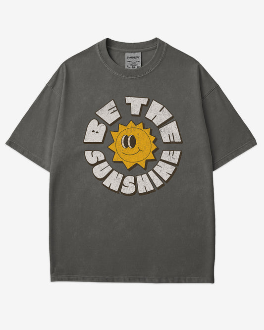 Flat lay pepper-colored Be The Sunshine shirt with a retro boho sun graphic.