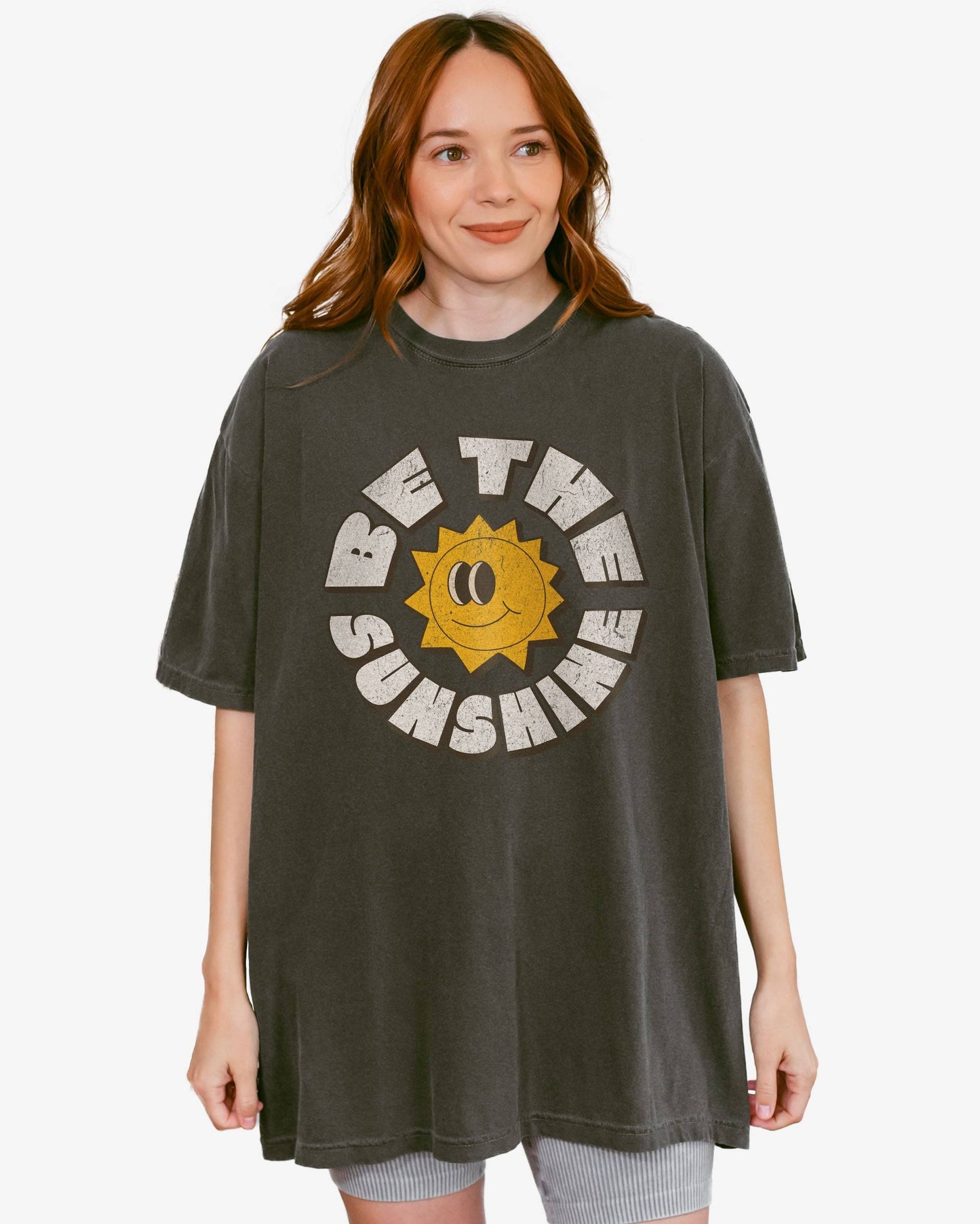 Woman wearing a pepper Be The Sunshine shirt with a retro boho sun graphic.